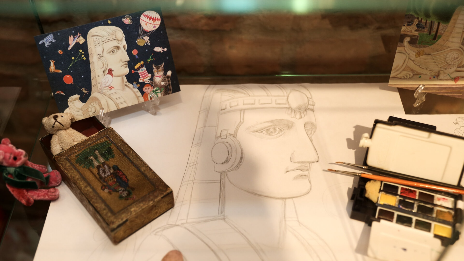Ilustrācija radošai darbnīcai “Sfinksas smaida noslēpums”, kuras centrā ir ar zīmuli skicēta sfinksas galva